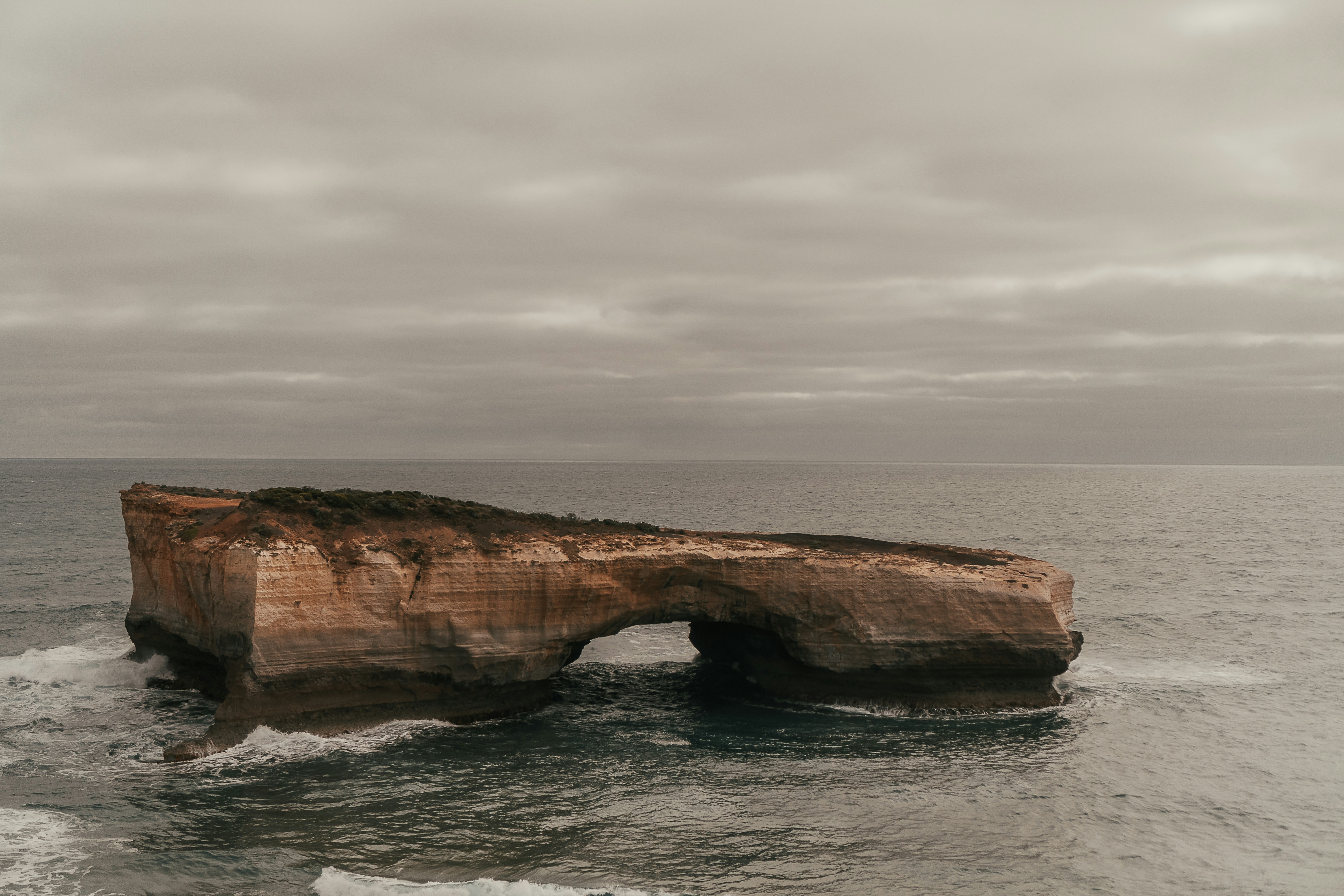 brown rock formation on sea under white clouds during daytime